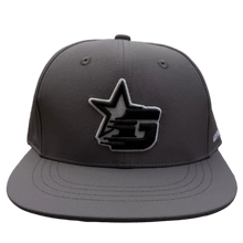 Load image into Gallery viewer, A dark gray snapback cap with a black and white embroidered star logo on the front, resting on a carpeted floor in a retail store.