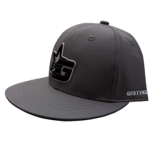 Load image into Gallery viewer, A dark gray flat-brim cap with a black and white graphic logo on the front and 'GRVTYKIDS' printed in white on the side, resting on a textured carpet in a retail store.
