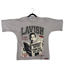 Load image into Gallery viewer, A light gray graphic t-shirt laid flat on a brown carpeted floor, featuring a newspaper collage print with the word 'LAVISH' and a portrait. A black hanger is attached to the collar.