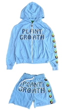 Load image into Gallery viewer, A light blue zip-up hoodie and matching shorts set laid out on a brown carpeted floor. The hoodie features 'PLANT CROATH' embroidered across the chest, colorful round buttons down one sleeve, and a white zipper.