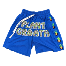Load image into Gallery viewer, Blue kids' athletic shorts with 'PLANT GROATH' printed across the front in a green-and-white patterned bubble font, white drawstrings, and embroidered carrot motifs down one side, laid flat on a tan carpet.