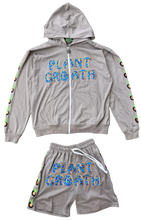 Load image into Gallery viewer, A two-piece gray zip-up hoodie and matching shorts set laid flat on a textured carpet. The front of both pieces feature the words 'PLANT GROTH' in blue with a small orange sun graphic.