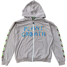 Load image into Gallery viewer, A gray zip-up hoodie laid flat on a textured carpet. The front has the words 'PLANT GROWTH' in blue and orange lettering, and there is a colorful circular pattern running along the sleeves.