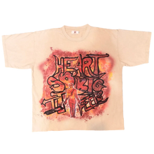 Load image into Gallery viewer, A cream-colored t-shirt with a red and black graffiti-style graphic reading 'HEART SHAPED TWENTY', laid flat on a gray carpet with slippers and clothing visible at the bottom.
