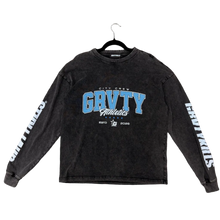 Load image into Gallery viewer, A dark washed charcoal long-sleeve t-shirt with 'GRAVITY Athletics' printed in blue and white on the front, laid flat on a textured gray carpet with a person's green socks and feet visible at the bottom.
