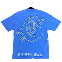 Load image into Gallery viewer, A blue graphic t-shirt laid flat on a brown carpeted floor. The shirt features a large white and yellow outline graphic on the front and the text 'E Turbis Annun' in white gothic font on the right side.
