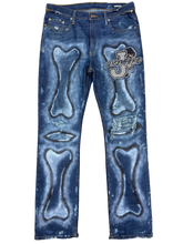 Load image into Gallery viewer, Pair of blue jeans with bone designs on a beige carpet

