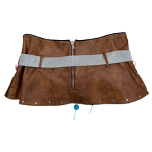 Load image into Gallery viewer, A brown faux-leather mini skirt with a central zipper and a wide white-and-black checkered waist belt, laid flat on a brown carpeted floor with black clogs visible at the bottom edge.

