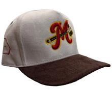 Load image into Gallery viewer, A baseball cap resting on a carpeted floor in a retail store. The cap has a white crown, a dark brown visor, and a red and yellow embroidered 'M' logo on the front.

