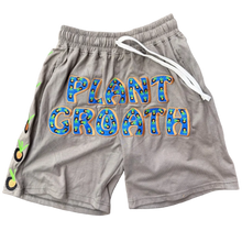 Load image into Gallery viewer, A pair of heather gray athletic shorts with a white drawstring and a colorful 'PLANT GROWTH' graphic on the front, laid flat on a textured carpet next to a matching gray zip-up hoodie.
