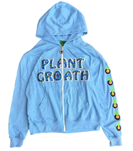 Load image into Gallery viewer, A light blue zip-up hoodie laid flat on a brown carpeted floor. The front has the words "PLANT GROWTH" in a colorful patterned font, and the right sleeve has a vertical row of small orange and green carrot graphics.

