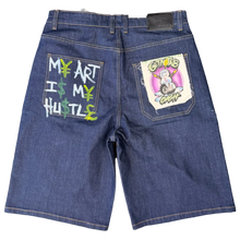 Load image into Gallery viewer, Pair of blue jeans with embroidered designs on a beige carpet
